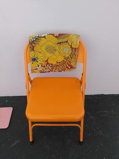 an orange folding chair with a piece of retro floral fabric foldeed over the back.