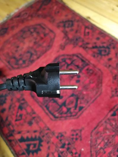 a close up image of a german two pin plug with a red patterened carpet in  the background